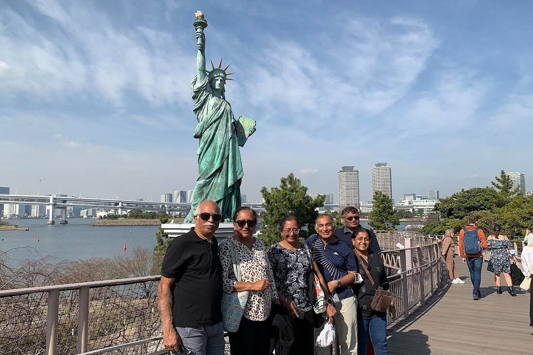 Travelers beside the Statue of Liberty replica on Odaiba, with Rainbow Bridge and the Tokyo waterfront